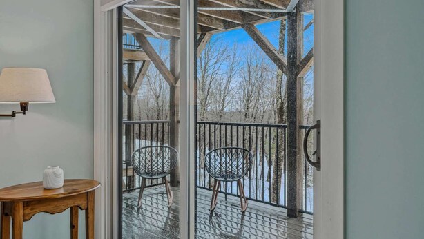 Une pièce comprenant une table en bois, une chaise, une lampe et une porte-fenêtre coulissante donnant sur une terrasse extérieure.