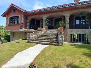 Una casa a due piani con una scala in pietra che conduce a un portico coperto, un garage e un prato curato.