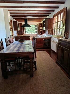 Un'area pranzo con tavolo e sedie in legno, una cucina con mobili in legno e vista attraverso una finestra.