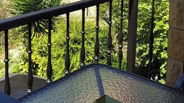 En balkon med gelænder, et lille bord og udsigt til en bygning med buevinduer og et tag med tagsten.
