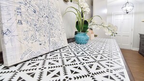 Une pièce avec un sol à motifs, une carte accrochée au mur et un vase rempli de fleurs blanches.