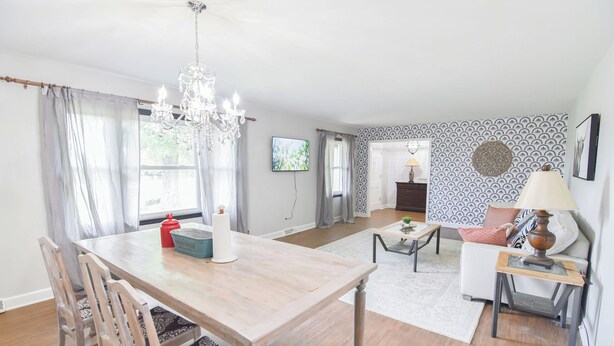 Un coin repas avec une table en bois, des chaises, un lustre et un téléviseur fixé au mur.