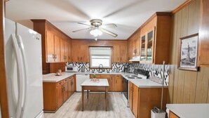 Une cuisine moderne avec des meubles en bois, un réfrigérateur blanc, un ventilateur de plafond et une fenêtre avec des stores.