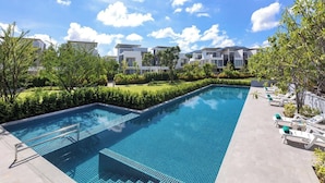 A rectangular swimming pool with a metal ladder, surrounded by a well-maintained hedge and trees. There are lounge chairs with cushions on the right side. - Laguna Park 4 Bedrooms Villa by NLA (Choeng Thale)