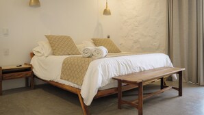 Una cama bien hecha con cabecera de madera, dos mesitas de noche y un banco.