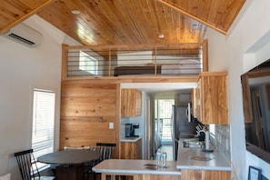 Un dormitorio estilo loft con techo de madera, comedor con mesa redonda y cocina equipada con electrodomésticos modernos.