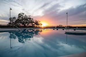 Una piscina con vista al atardecer, rodeada por una valla y dos farolas.