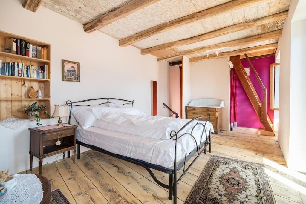 Une chambre avec un plancher en bois, un cadre de lit en métal, une table de chevet avec une lampe, une bibliothèque et un escalier menant à une autre pièce.