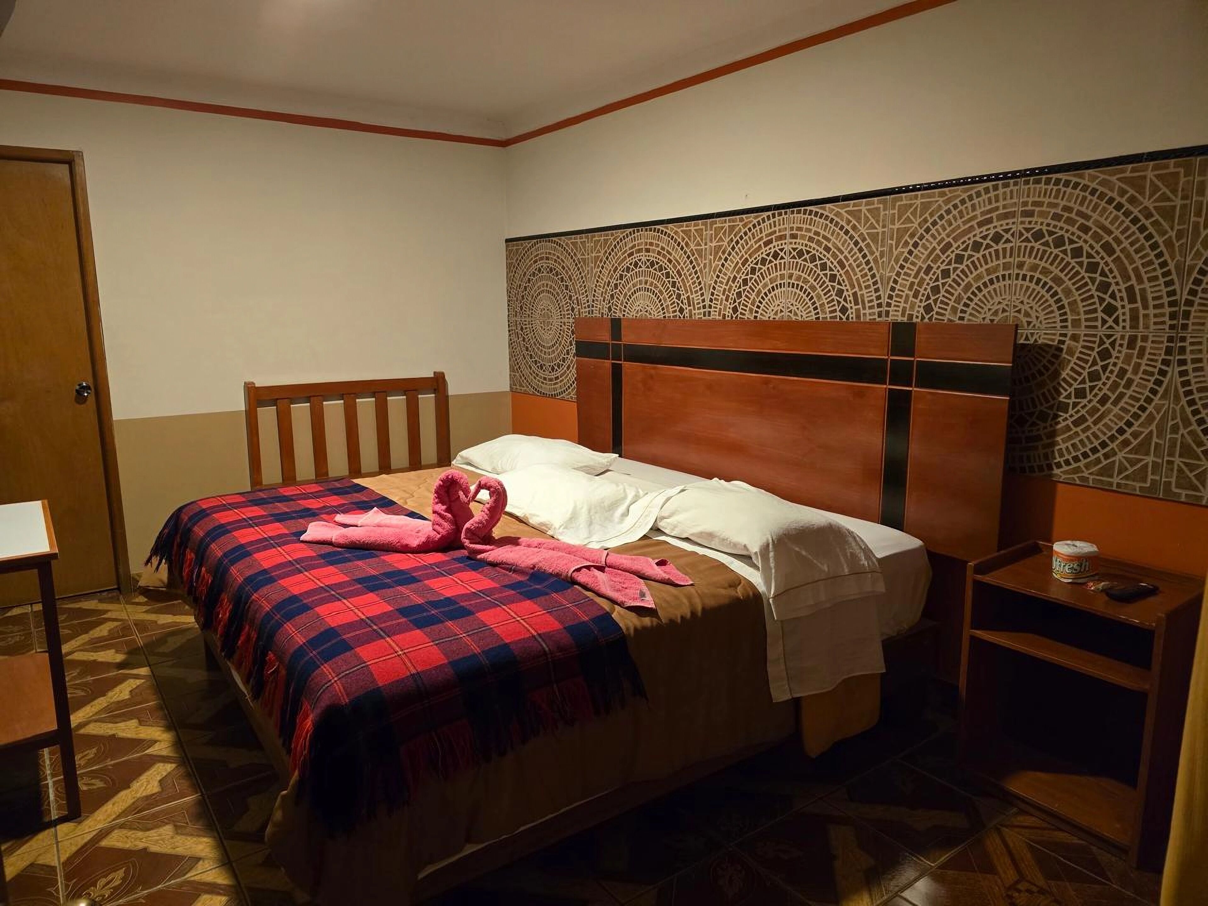 Une chambre d’hôtel avec un lit, une tête de lit en bois, une table de chevet et une petite table.