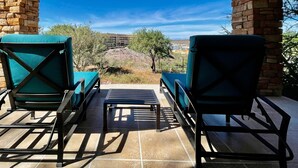 Eine Terrasse mit zwei grünen Sitzgelegenheiten und einem kleinen Tisch, vor einer Steinmauer mit Blick auf ein Gebäude und die Landschaft in der Ferne.