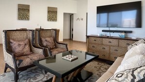 Ein modernes Wohnzimmer mit zwei Polstersesseln, einem Glastisch, einer Couch, einem flachbildfernseher an der Wand und einem dekorativen Schrank.