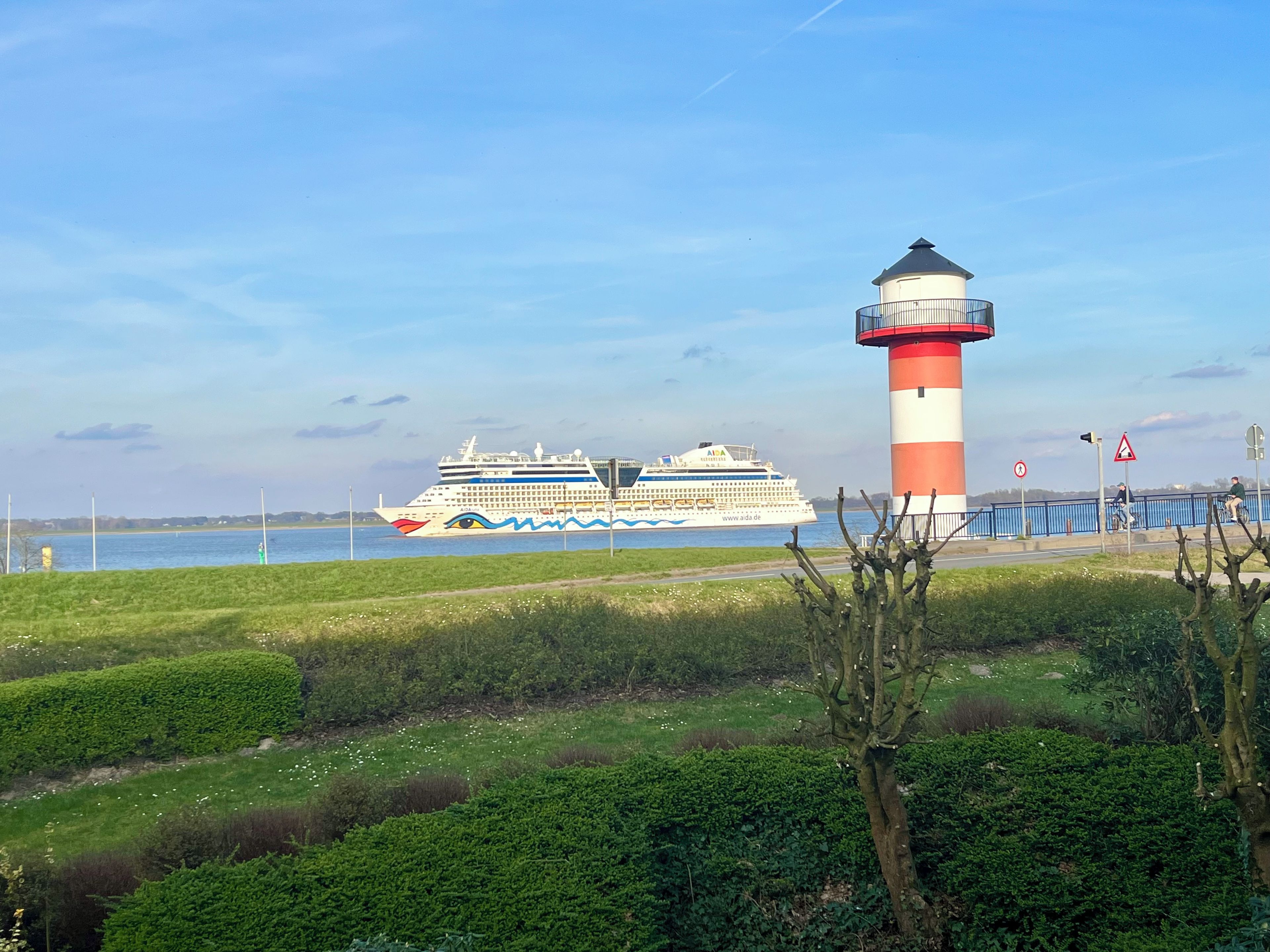Una nave da crociera ormeggiata vicino a un faro, con cielo sereno.