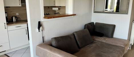 Een moderne woonkamer met een bank, een keuken met kastjes en een aanrecht, en een spiegel aan de muur.