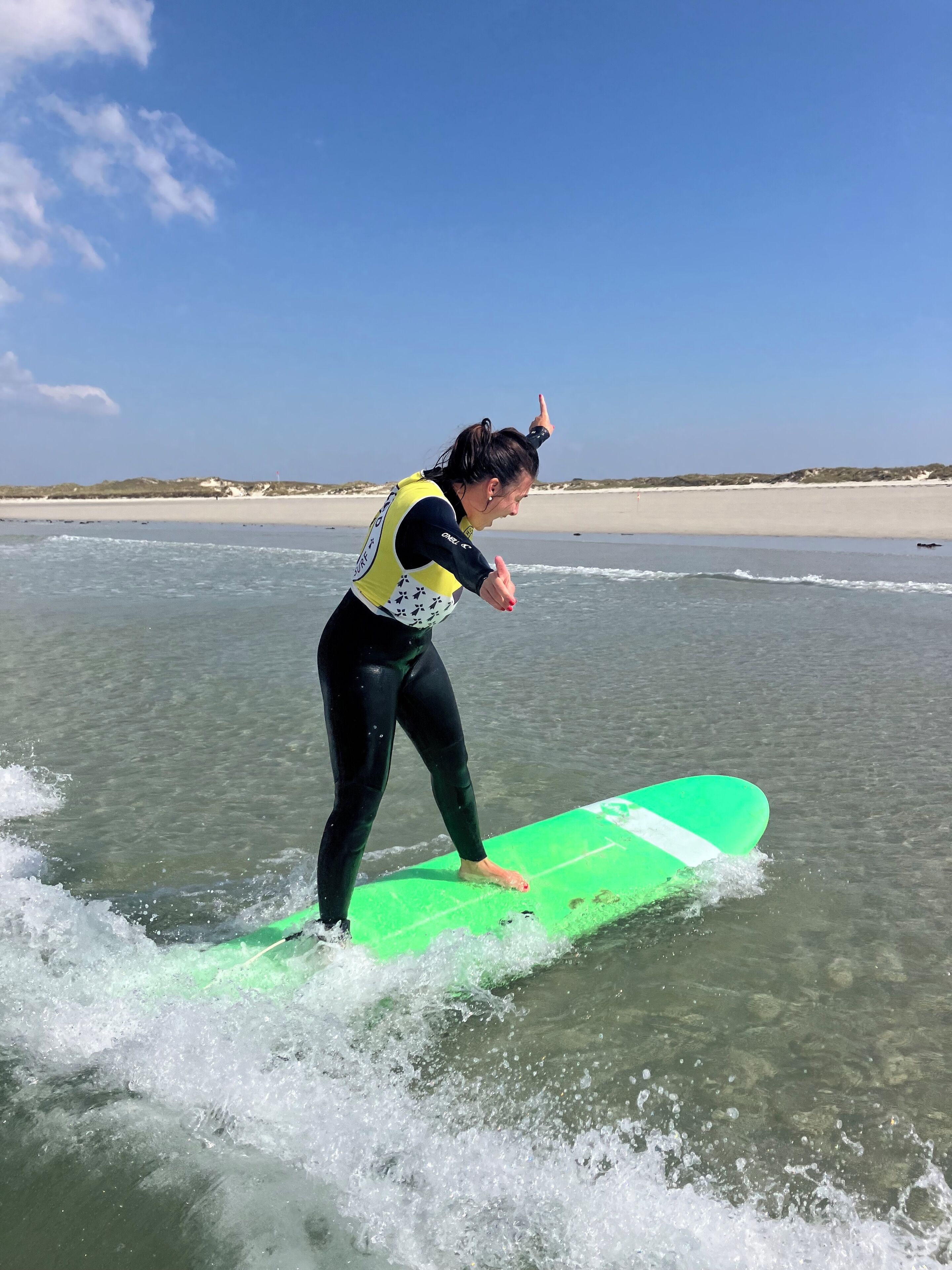 A person in a wetsuit standing on a green surfboard in shallow water.