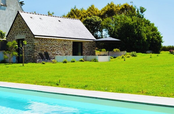 Un bâtiment en pierre avec un toit en pente, une piscine et une cour gazonnée.