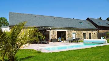 A stone building with a swimming pool, outdoor seating, and a covered patio area.