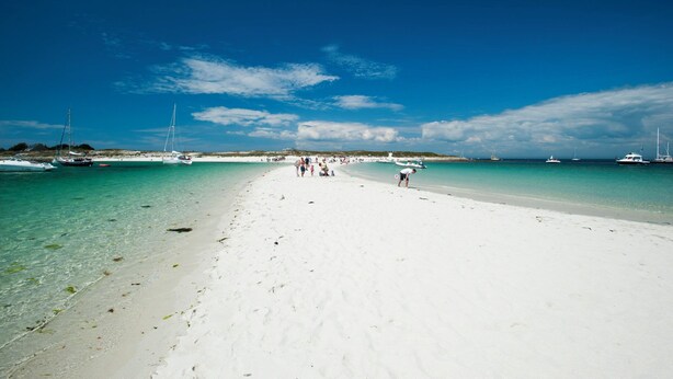 A beach with clear turquoise water and white sand, boats in the background, and people on the shore. - La Maison de Célestine Bord de mer et Piscine (Plonéour-Lanvern)