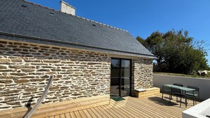 A stone building with a wooden deck and outdoor seating area. - La Maison de Célestine Bord de mer et Piscine (Plonéour-Lanvern)