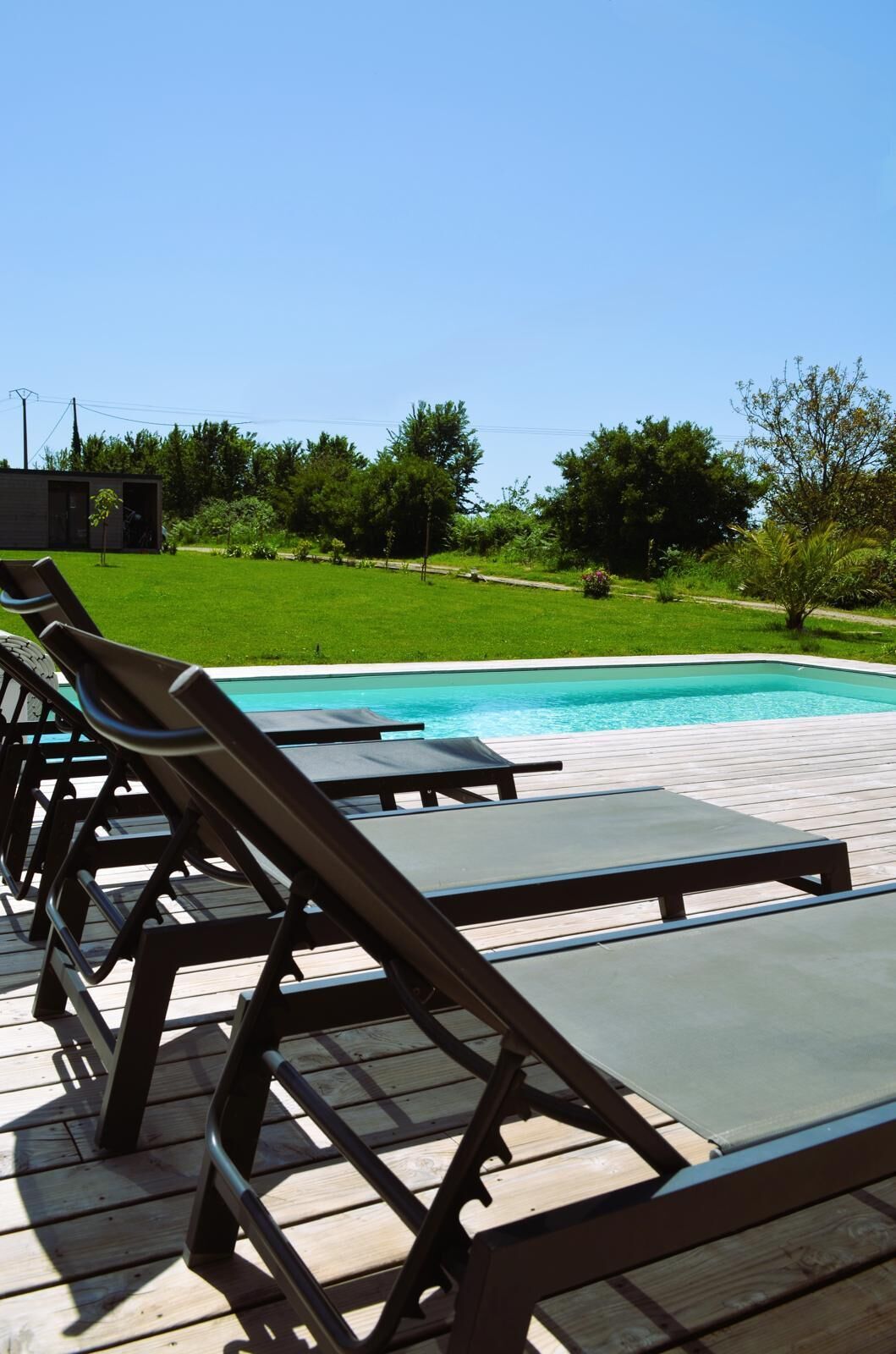 Área da piscina com espreguiçadeiras e deck de madeira.