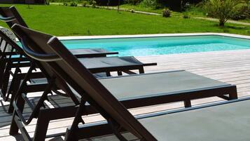 Área da piscina com espreguiçadeiras e deck de madeira.