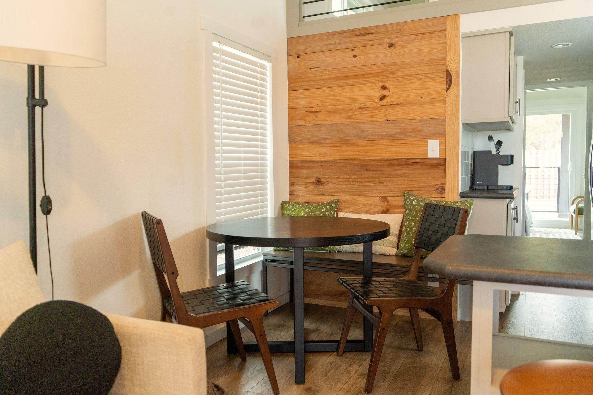 A dining area with a round table and four chairs, a lamp, and a wooden wall panel.