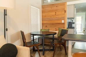 A dining area with a round table and four chairs, a lamp, and a wooden wall panel. - Mingo Cabin - Modern Cabin by Resort Pool, King Loft, Sleeps 6, Dogs OK (Wimberley)