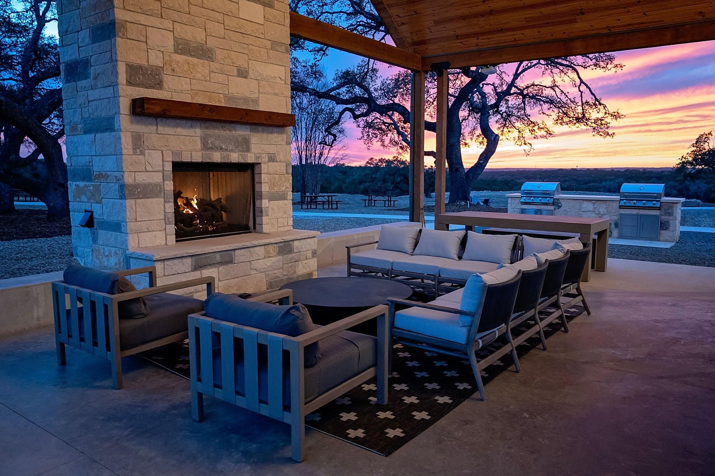 An outdoor patio with a stone fireplace, seating area, and a view of the sunset.