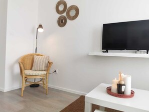 Relax in a serene space with a wicker armchair, floor lamp, and flat-screen TV.