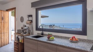 A kitchen with a large window overlooking the sea, a sink, a coffee maker, and a fruit bowl. - Finca los Paseros Cómpeta by Ruralidays (Málaga)