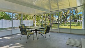 A covered patio with a table and chairs, large windows, and a view of a fenced yard with trees. - King's Bay Point Retreat - Water View (Crystal River)