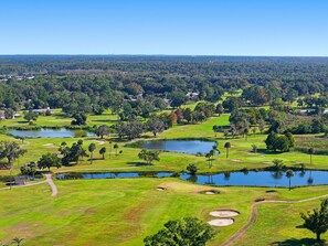 A golf course with multiple ponds, trees, and a clear sky.