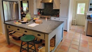 Una cocina con gabinetes grises, una isla grande con taburetes, una estufa y un refrigerador.