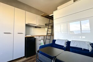 Una cocina compacta con armarios blancos, un refrigerador negro y un sofá azul con una mesa.