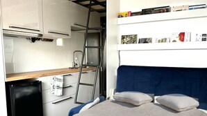 Quarto compacto com cama, escrivaninha, escada, mini-geladeira e estante.