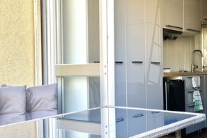 A balcony with a glass table, a sofa with cushions, and a kitchen area with cabinets and a refrigerator. - SE078- Senigallia, new sea front studio at the ''Pyramids'' (Senigallia)