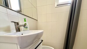 Uma casa de banho com uma pia branca, um espelho, uma sanita e uma janela com cortina.