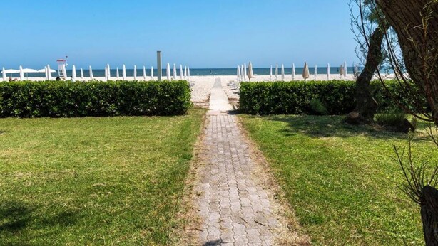 Un chemin pavé mène à une plage où se trouvent des parasols blancs et un poste de surveillance des sauveteurs.