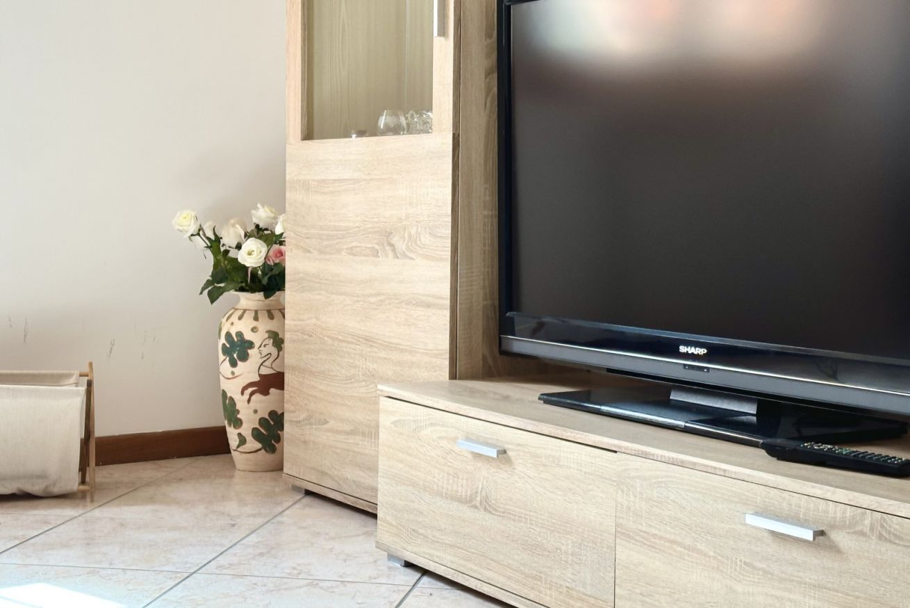 Un soggiorno moderno con televisione a schermo piatto, mobiletto in legno e un vaso decorativo con fiori.