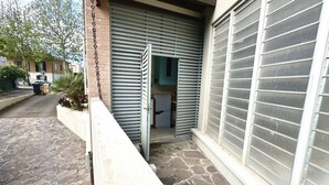 A closed metal shutter door, a stone-paved entrance, and a small garden area with plants. - SE076 - Senigallia, three-room apartment convenient to services (Senigallia)