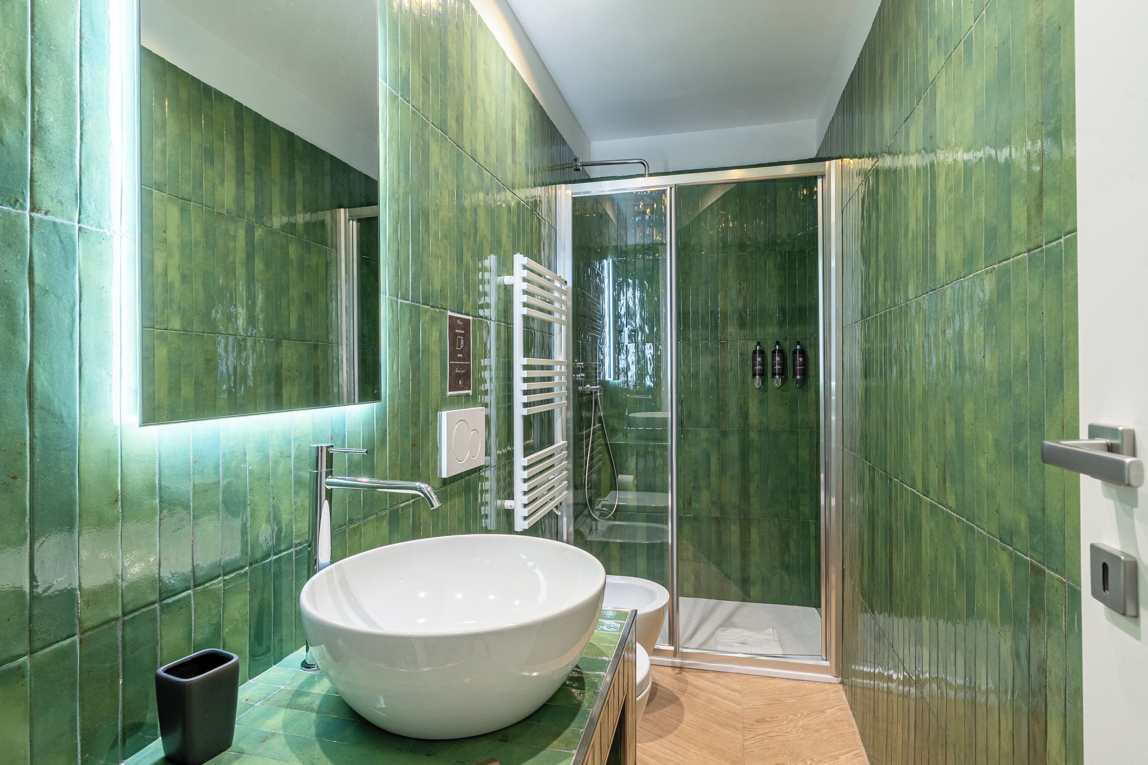 Une salle de bain moderne avec un grand lavabo blanc, une douche en verre et des murs recouverts de carreaux verts.