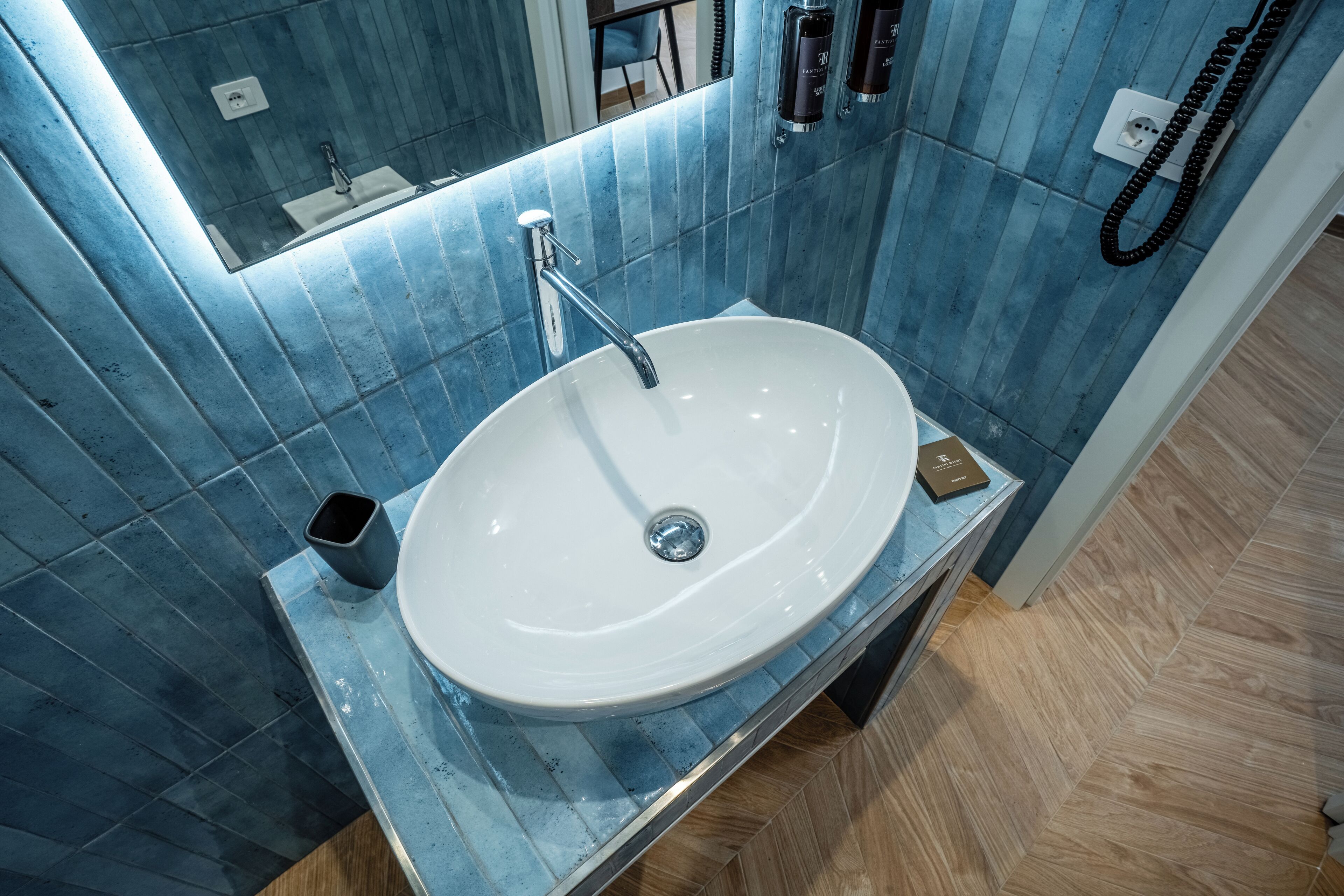 A bathroom with a white sink, blue-tiled walls, and a wooden floor.