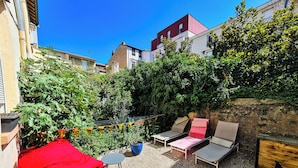 Un patio exterior con asientos, un paño rojo y una maceta azul.