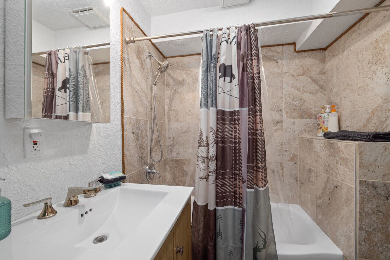 Een badkamer met een wit wastafel, een spiegel, een douche met gordijn en een handdoekhouder.