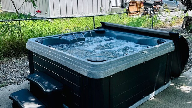 Ein Whirlpool mit integriertem Sitzplatz und Stufen, umgeben von einem Zaun und Pflanzen.