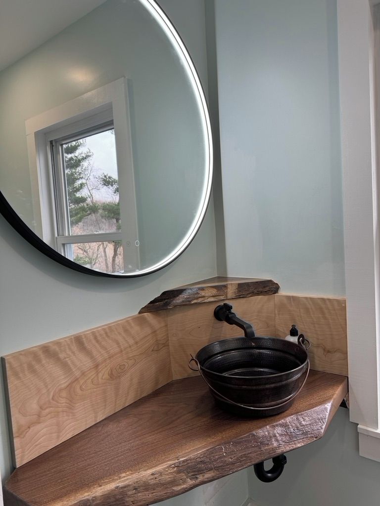 Une salle de bain avec un meuble-lavabo en bois, un miroir rond et un lavabo noir.