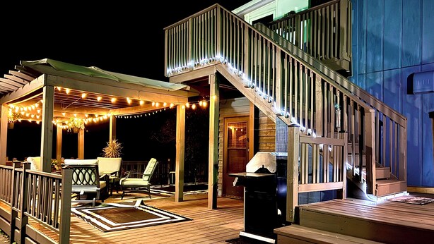 A wooden deck with a covered seating area, a staircase, and string lights.