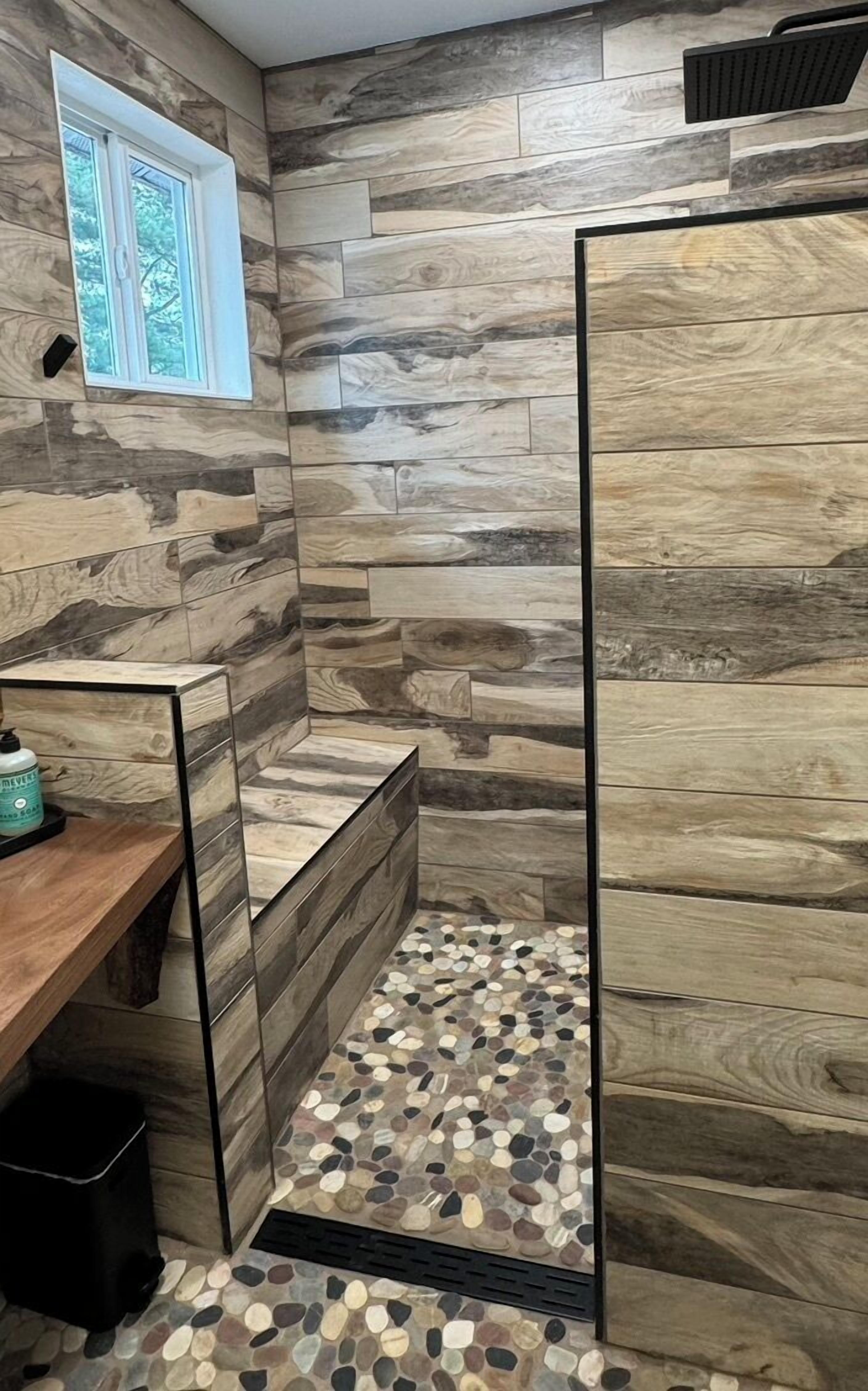 Un baño con diseño de pared de madera, ventana y suelo con estampado de guijarros.