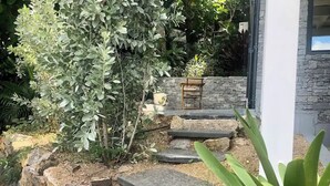 A garden with stone steps leading to a wooden bench, surrounded by various plants and a stone wall.