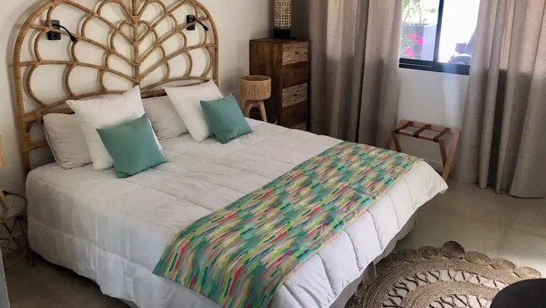 A neatly made bed with a white duvet and colorful throw blanket, a wooden headboard, and a small wooden side table with a lamp.