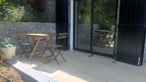 An outdoor patio with a stone wall, wooden furniture, and a glass door leading to a garden.